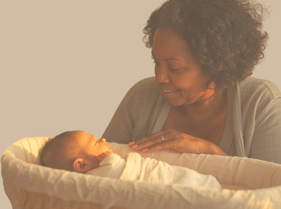 A grandmother smiling down at her sleeping newborn grandchild